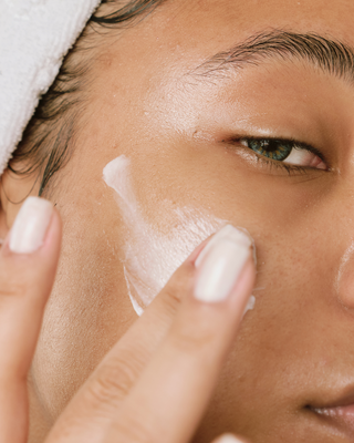 Person applying cream to their face with a finger.