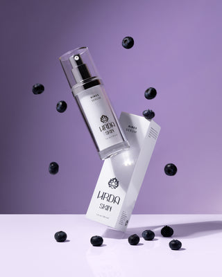 Hrda Skin Ribes Serum and packaging box with tossed blueberries on light purple background