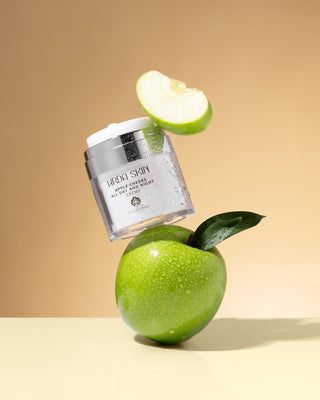 Hrda Skin Apple Cheeks All Day and Night Creme between a green apple and apple slice on gold background.